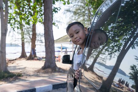 Asian boy extends his face out of the car Which parked by the seaの写真素材