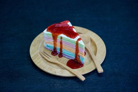 Rainbow crepe cake with strawberry jam on wooden plateの写真素材