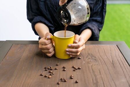 Person pouring coffee in yellow cup that has hands holdの写真素材