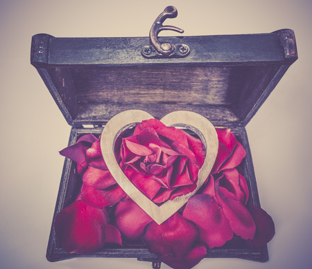 Wooden heart on rose petals in a coffer -  Romantic image with a wooden coffer filled with red rose petals on top of which lies a heart, as a treasure.の写真素材