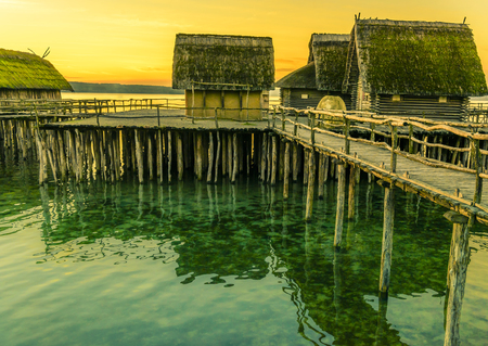 Fishing huts made from wood, clay and thatched roof, suspended on stilts over a lake water, with the beautiful yellow sunset in the backgroundの写真素材