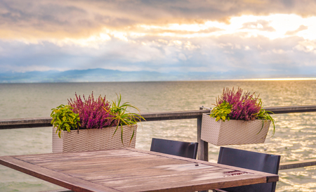 Conceptual image with an empty table, on a terrace, on the shore of the Bodensee lake, at sunset.の写真素材