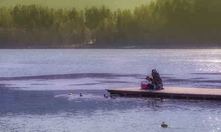 Slovenian young woman reading a book and relaxing in nature on a wooden pier on the Bled lake, Sloveniaの写真素材