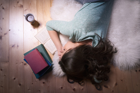 Upside down image with a young brunette girl that fell asleep reading a book, lying on a white fur direct on the floor.の写真素材