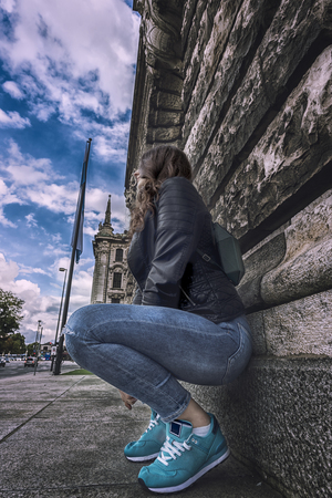 Street photography in Munich, Germany with young woman modern dressed, leaning on an old building wallの写真素材