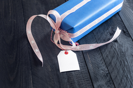 Chic present, wrapped in blue paper and tied with pink ribbon and bow, with an empty label attached to it, on a black wooden table.の写真素材