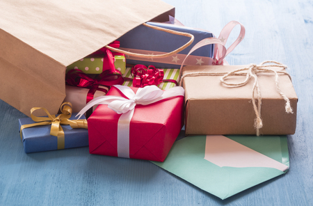 Colorful gift boxes coming out on a blue wooden table from a paper shopping bagの写真素材