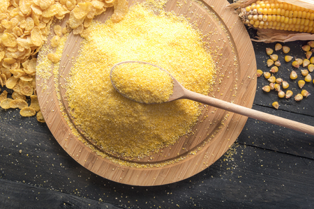 Rustic image with a wooden spoon full of corn flour on top of a wooden board, surrounded by corn flakes, grains and corn cob, on a black wooden table.の写真素材