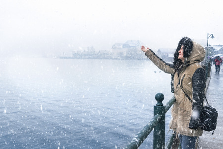Winter destinations theme image with a woman standing on the Hallstatter lakeshore, catching snowflakes and enjoying the snowfall, in Hallstatt town, Austria.の写真素材