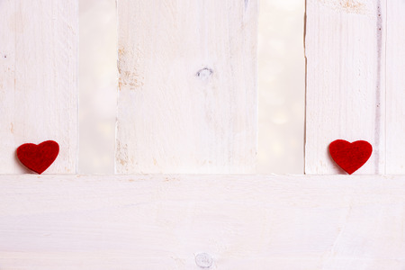 Cute little red hearts, displayed one on the left and one on the right of a white wooden fence. A concept of love, breakup, romance, valentine day.の写真素材