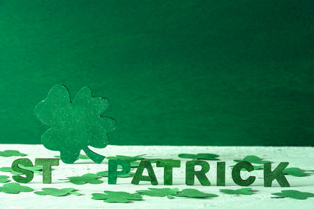 The words St Patrick written in green wooden letters and a big green clover in the back, surrounded by paper shamrocks, on a green wooden background.の写真素材