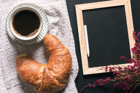 Breakfast table with a cup of coffee and a croissant on a vintage kitchen towel, near an empty...