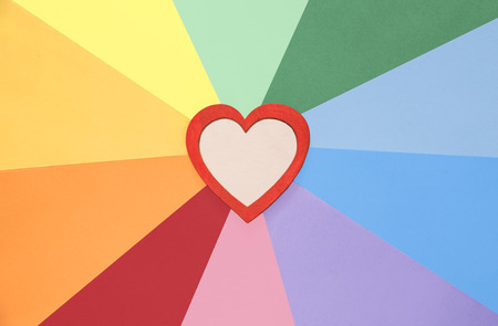 Cheerful image with a red wooden heart with space for text in the interior, placed on paper background in rainbow colors.の写真素材