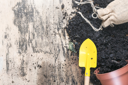 Potting plants in spring concept with a flower pot overturned, full of soil, a gardening spade and a jute sack, on a vintage wooden workspace.の写真素材