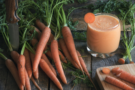 Healthy eating concept with a glass of fresh carrots smoothie, surrounded by a bunch of carrots with...