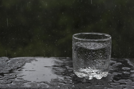 Conceptual image with a glass abandoned in the rain, to be filled with water, surrounded by...
