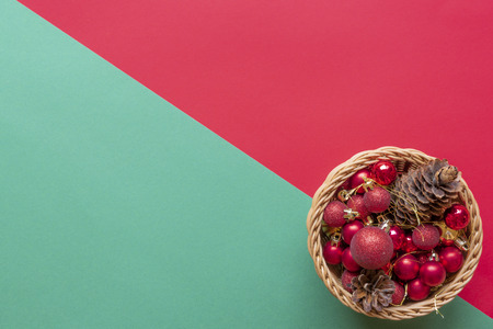 Pine cones and christmas globes in a wooden basket on a red and green backgroundの写真素材