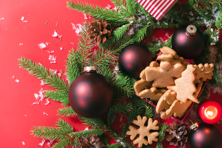Above view of a box with ginger Xmas cookies, red balls, green fir twigs, on a red background with snowflakes. A Christmas banner or greeting card.の写真素材