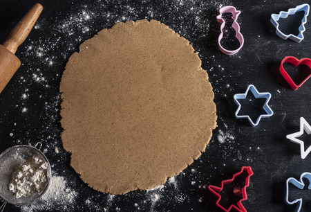 Black wooden table above view with multicolored cookie cutters and gingerbread batterの写真素材