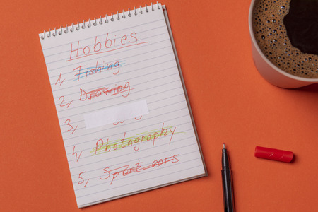 Hobbies list handwritten on a notebook page. Above view with an orange colored office desk.の写真素材
