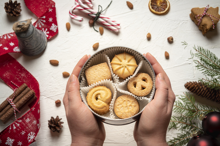Round box filled with cookies in a woman's hands. Above view of a table full of Christmas goodies and decorationsの写真素材