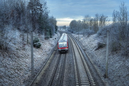 German passenger train traveling through snowy nature and frozen trees, at sunrise. Winter travel context. Modern public transportation.の写真素材