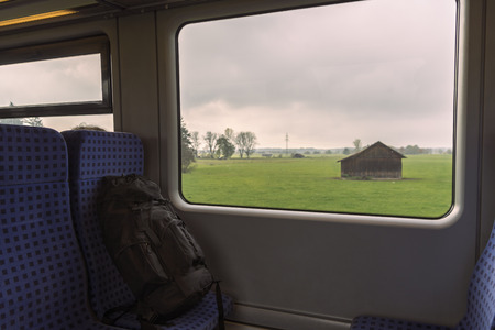 Rucksack on the train seats near the window. Interior train with a view over bavarian landscapes on the windowの写真素材