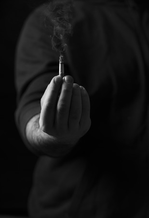 Smoking cigar in a man's hand. Quit smoking concept. Monochrome image in low lightの写真素材