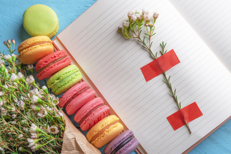 Open notebook with flower stuck on it, multicolored macaroons and tiny white flowers bouquet. Above view of french dessert and spring flowers. Women day frame.の写真素材