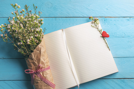 Open blank notebook on a blue desk and a bouquet of spring flowers on it. Mothers day frame. Woman...