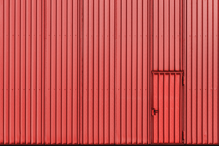 Warehouse facade of coral color, metal sheet wall, and door. Aluminum panel industrial wall and door. The metal door of an industrial building.の写真素材
