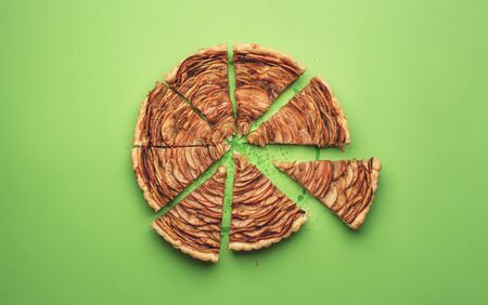 Traditional American dessert, a tasty apple pie cut in slices on a green paper background. Flat lay of autumn sweet pastry. Minimal style.の写真素材