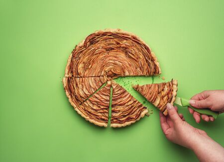 Woman taking a slice of rose flower-shaped apple pie on a knife, on a green paper background. Flat...