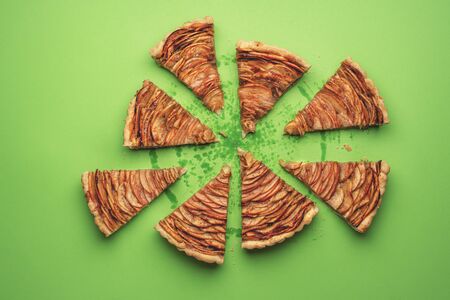 Apple pie cut in pieces on a green paper background. Above view of tasty American pie. Portions of...