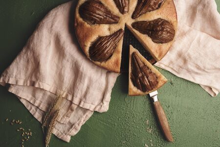 Soft cake with whole pears on a kitchen towel. Above view with a sliced fruit pie. Single slice of...