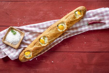 Loaf of french bread filled with eggs, freshly baked,  on a kitchen towel and wooden table. Above view of breakfast table. Flat lay with baked eggs.の写真素材