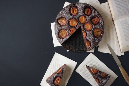 Autumn dessert with plums and chocolate on old book pages on black background. Above view of plums...