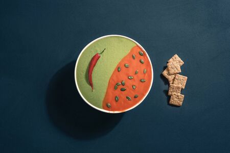 Tomato a spinach cream soup in a bowl with seeds and crackers, on a blue background. Above view of a healthy meal. Flat lay of a vegetarian dish.の写真素材