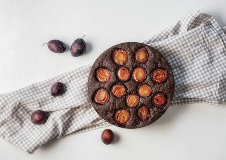 Fruitcake with plums and cocoa on a kitchen towel and white tabletop. Above view of autumn dessert. Flat lay of plum pie. Tasty fruit tart.の写真素材