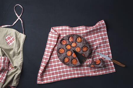 Kitchen table with plums tart and chocolate on a red towel and black table. Above view of plum pie...