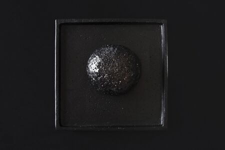Black hamburger bun bread with sesame on a black tray and tabletop. Minimal image of weird bread....