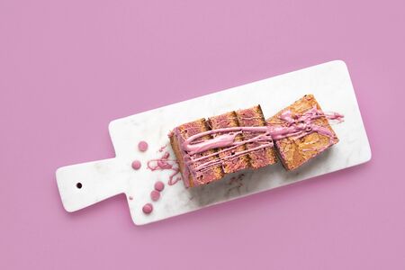 Ruby chocolate dessert in slices displayed on a white cutting board and pink background. Above view...