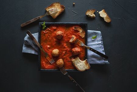Meatballs in tomato sauce and a  black plate with toasted bread and many forks. Party food. Above view of dinner setting for many people. Swedish foodの写真素材
