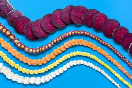 Root vegetables sliced and symmetrically arranged on a blue background.の写真素材