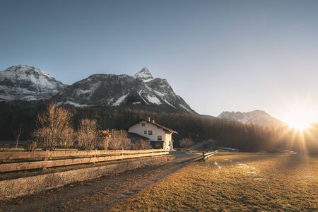 Snowy Alps mountains peaks and Austrian farm in the evening light, on a sunny day of winter, in Ehrwald, Austria. December sunset scenery.の写真素材