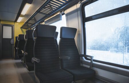 Winter traveling concept with a german train interior with black seats, in a row, and a window view...