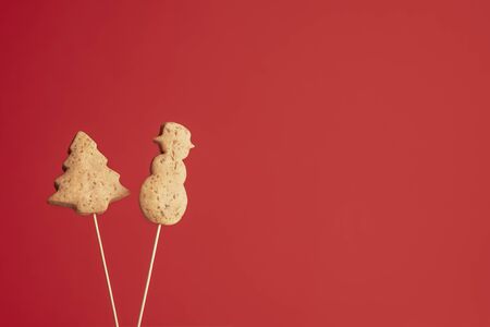 Christmas tree and snowman shape cookies on skewers, on red background. Xmas traditional gingerbread cookies. American Christmas famous dessert.の写真素材