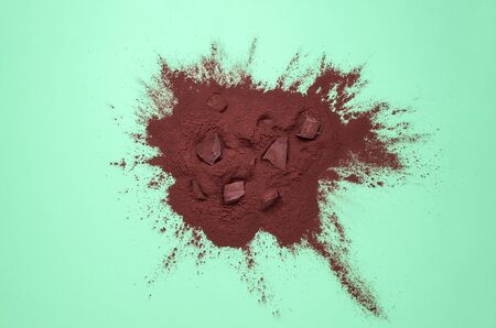 Pieces of milk chocolate on a pile of cocoa powder on a green paper background. Above view of...
