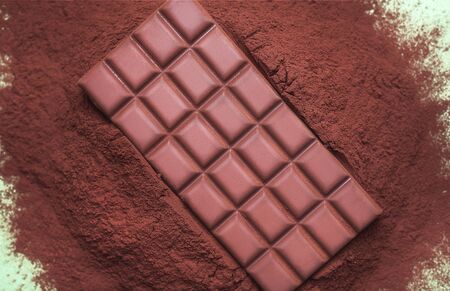 Chocolate bar with squares on a pile of powder cocoa on a green background. Above view of brown milk...