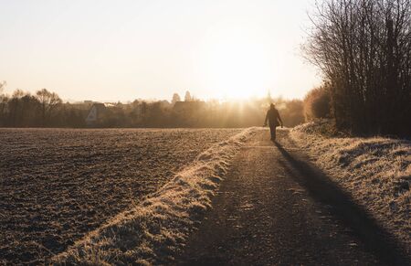 Man silhouette wandering on countryside alley at sunrise, on cold winter morning. Frozen nature...